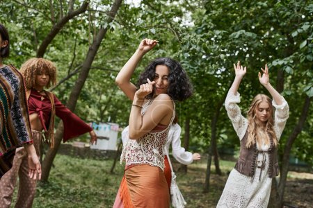 joyful multiracial woman in boho clothes looking at camera and dancing in retreat center