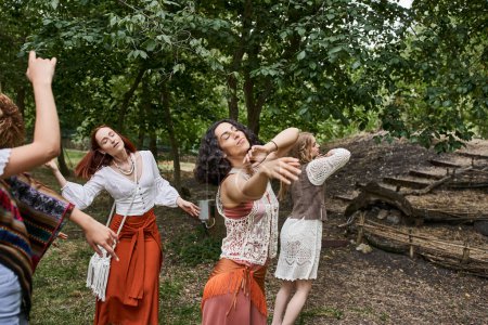 multiethnische Freundinnen in stilvoller Kleidung tanzen mit geschlossenen Augen im Outdoor-Retreat-Zentrum