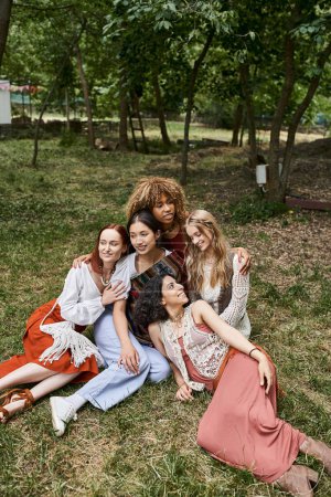 Photo for Smiling interracial women in stylish boho outfits while sitting together outdoors in retreat center - Royalty Free Image