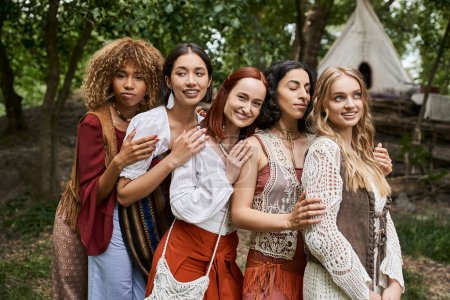Photo for Trendy and carefree interracial girlfriends in boho outfits hugging outdoors in retreat center - Royalty Free Image