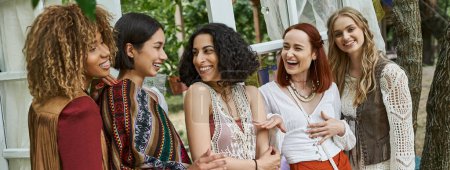 carefree multiethnic girlfriends in boho outfits talking in modern retreat center, banner