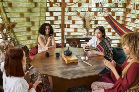 Rückzugskonzept für Frauen, positive multiethnische Freundinnen, die Tee trinken und sich am Holztisch unterhalten