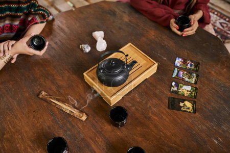 Photo for Cropped view of girlfriends with tea cups, teapot, tarot cards and palo santo, women retreat concept - Royalty Free Image