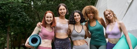 Rückzugskonzept für Frauen, zufriedene multiethnische Freundinnen mit Yogamatten, die im Park in die Kamera schauen