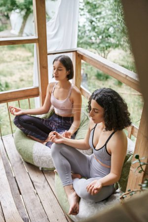 women retreat concept, multiethnic women meditating in lotus pose in cottage of retreat center