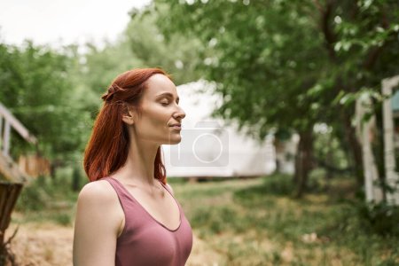 happy redhead woman meditating with closed eyes in retreat center outdoor