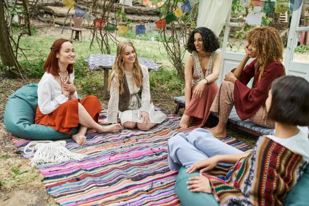 happy multiethnic girlfriends talking on colorful blanket in park, women retreat concept