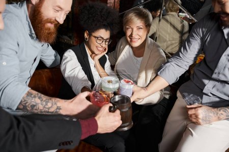 fröhliche multiethnische Kollegen, die nach Feierabend in der Bar Gläser mit Cocktails klappern und Spaß haben