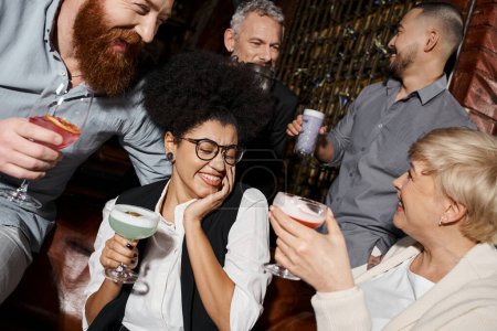 Foto de Mujer afroamericana riendo con los ojos cerrados cerca de amigos multiculturales pasar tiempo en el bar - Imagen libre de derechos