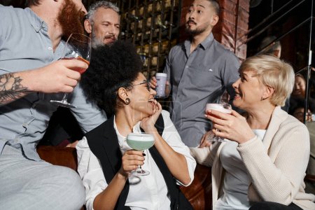 fröhliche multikulturelle Kollegen trinken Cocktails und unterhalten sich in der Bar, nach der Arbeit entspannen