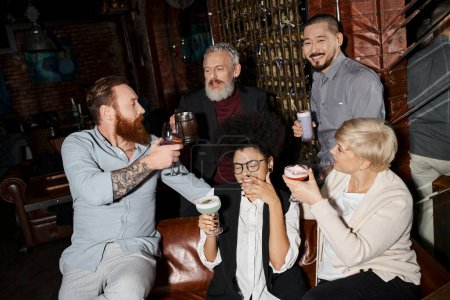 Freizeit multikultureller Kollegen, bärtige tätowierte Männer, die in einer Bar neben fröhlichen Frauen anstoßen