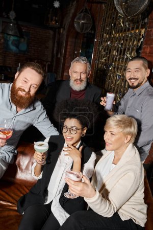 overjoyed african american woman laughing near multicultural colleagues with drinks in cocktail bar