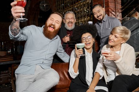 Téléchargez les photos : Amis multiethniques excités tenant des boissons et riant dans un bar à cocktails, s'amusant après le travail - en image libre de droit