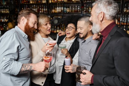 alegres colegas multiculturales sosteniendo vasos con bebidas y hablando en un bar de cócteles después del trabajo