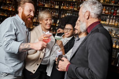 Téléchargez les photos : Satisfaits multiethniques compagnons de travail griller avec des cocktails tout en passant du temps dans le bar après le travail - en image libre de droit