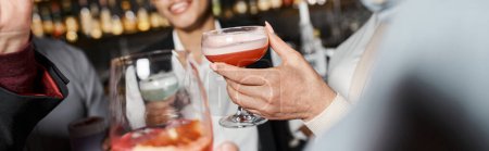 vista recortada de amigos de trabajo multiétnicos sosteniendo vasos con bebidas alcohólicas en el bar de cócteles, pancarta