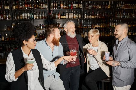 Frau mittleren Alters blickt in die Kamera neben positiven multikulturellen Freunden, die Cocktails in einer Bar trinken