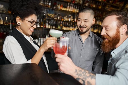 cheerful african american woman clinking glasses with multiethnic colleagues in cocktail bar