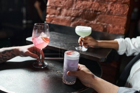 Téléchargez les photos : Vue recadrée de la femme afro-américaine et des hommes tatoués avec des cocktails au bar, loisirs après le travail - en image libre de droit