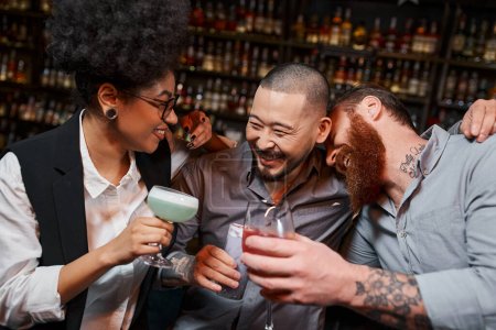 überglückliche multiethnische Arbeitskollegen mit Cocktails, die sich umarmen und lachen in der Bar, Freizeit und Spaß