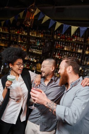 bärtige Männer, die eine lachende Afroamerikanerin während einer Afterwork-Party in einer Bar anschauen