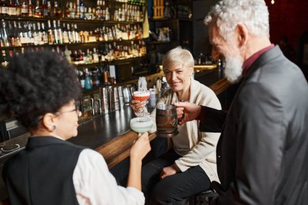 positive multiethnic women and bearded man relaxing in cocktail bar after work, corporate party