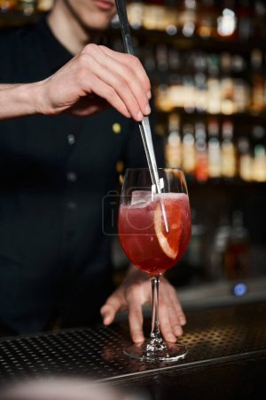 Téléchargez les photos : Vue recadrée du barman en ajoutant une tranche d'orange fraîche dans un cocktail alcoolisé au bar, création de boissons - en image libre de droit