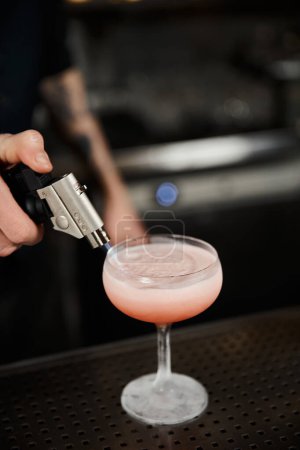 abgeschnittene Ansicht des Barkeepers mit Karamellisierer bei der Zubereitung von Milchpunsch in der Bar, Cocktail-Artistik