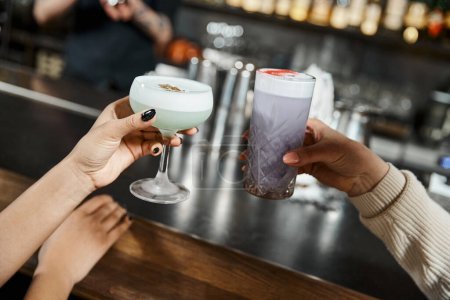 abgeschnittene Ansicht multiethnischer Kolleginnen mit leckeren Cocktails in der Bar nach Feierabend