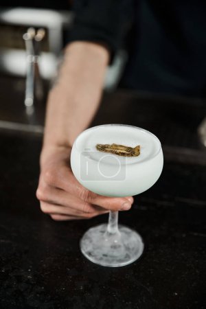 cropped view of bartender presenting glass of milk punch with kiwi slice, cocktail hour in bar