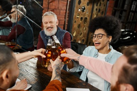 fröhliche multiethnische Arbeitsfreunde, die nach Feierabend in der Bar Bierflaschen klappern