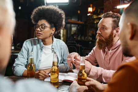 Téléchargez les photos : Amis de travail attentifs multiethniques assis près des bouteilles de bière dans le pub lors de la discussion du nouveau projet - en image libre de droit