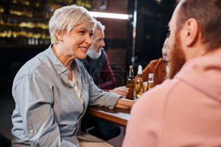 Photo for Happy middle aged woman listening to bearded colleague near blurred multiethnic team talking in pub - Royalty Free Image