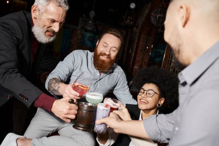 bärtige tätowierte Männer und afrikanisch-amerikanische Frau beim Gläserklirren in der Cocktailbar, After-Work-Spaß