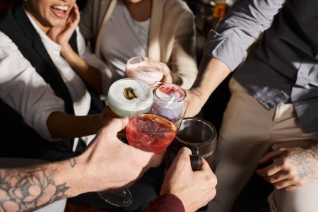 vista recortada de colegas multiétnicos tintineando vasos con deliciosos cócteles en el bar, tiempo de fiesta