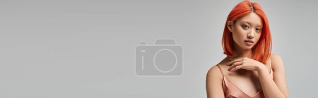 portrait of pretty young asian woman in silk slip dress looking at camera on grey background, banner