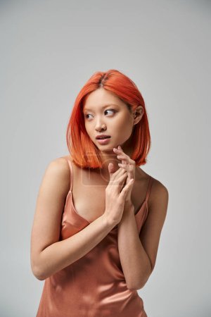 Photo for Portrait of dreamy young asian woman with red hair posing in silk slip dress on grey background - Royalty Free Image