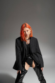 stylish asian woman with red hair posing in bold attire with latex boots and blazer on grey backdrop mug #673632432