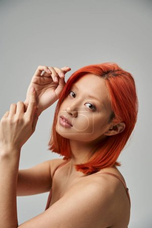 portrait of pretty asian woman with dyed hair looking at camera on grey background, natural beauty