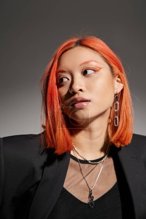 portrait of pretty asian woman with red hair and piercing in nose looking up on grey backdrop