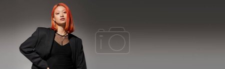portrait of stylish asian and young woman in blazer looking at camera on grey background, banner