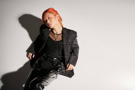 top view of asian woman with closed eyes and red hair posing in bold attire on grey background