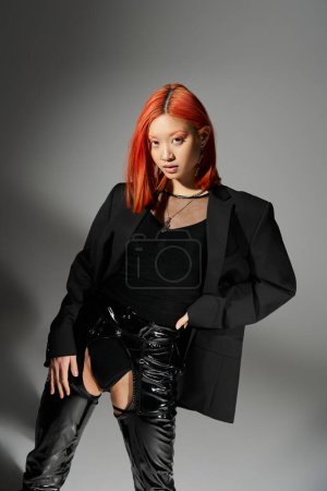 asian model with red hair posing with hand on hip, standing in latex boots and oversized blazer
