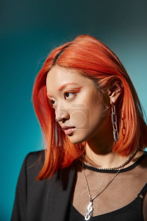 asian model with red hair and nose piercing posing in oversized blazer on blue backdrop, accessories