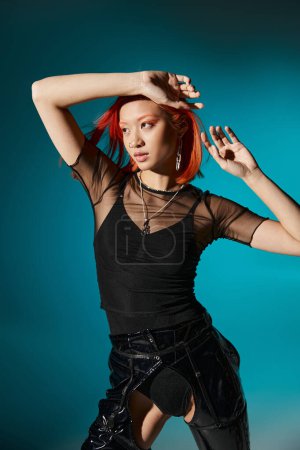 young asian woman with piercing posing in black latex and transparent blouse on blue backdrop