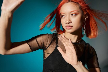 Téléchargez les photos : Jeune femme asiatique avec piercing posant contre le vent en chemisier transparent sur fond bleu, geste - en image libre de droit