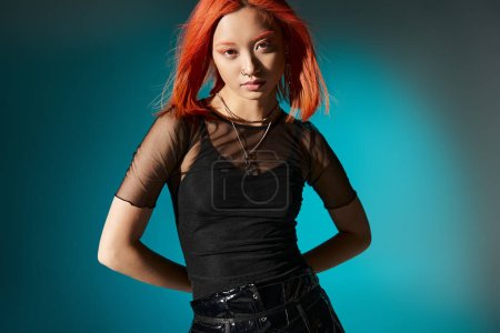 sassy asian model with piercing posing in black latex pants and transparent blouse on blue backdrop