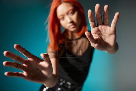 Foto mit Fokus auf Hände, junge asiatische Frau mit roten Haaren auf verschwommenem und blauem Hintergrund,