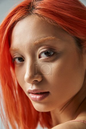 close up of asian young woman with natural makeup and red hair looking at camera, soft skin