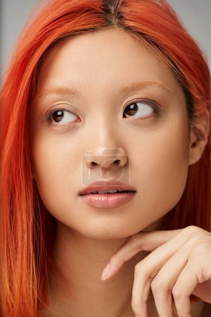 Nahaufnahme Porträt einer hübschen und jungen Asiatin mit perfekter Haut, die vor grauem Hintergrund tagträumt